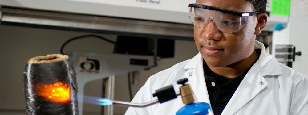 Student wearing goggles and a lab coat while using a propane torch in a Materials Science and Engineering lab